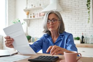 Older Woman Using Calculator and Reading a Paper for Personal Finances.